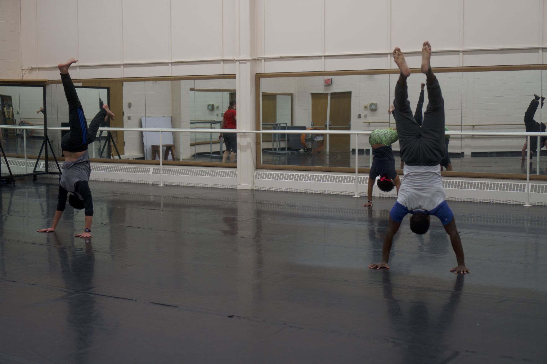 3 people do handstands on a rubber mat in front of a wall of mirrors in Robinson Center